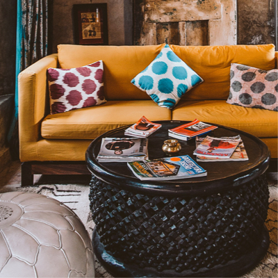 a faded orange couch with poka-doted pillows placed on the seat, all different colors, with a coffee table in front with magazines left on top