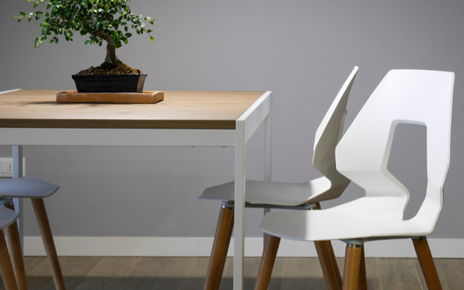 a very structured, art-deco style chair that is white with wooden legs and accompanied by a beautiful wooden surface table with a bonsai tree on top